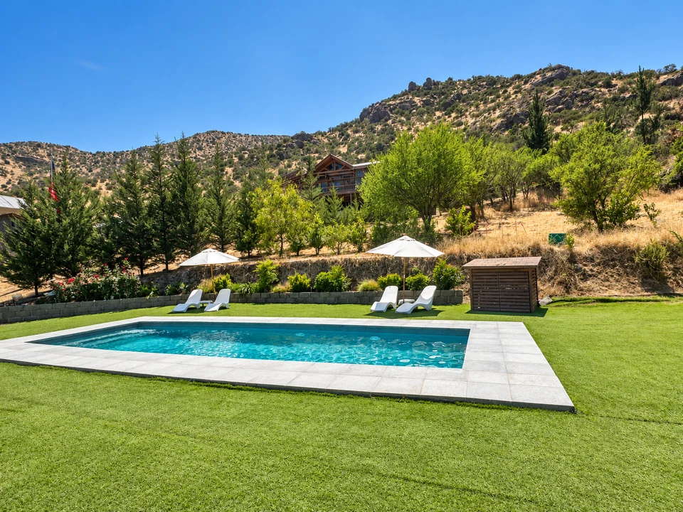 Piscina de la celebración, reposeras y vegetación al pie de los cerros de Lampa